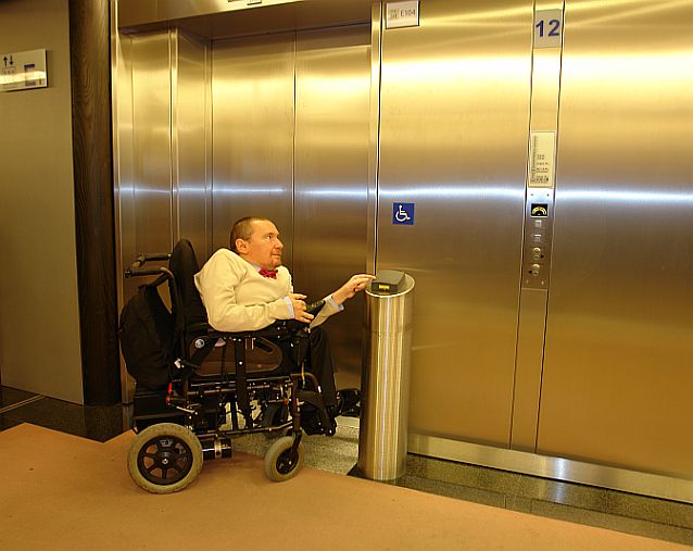 Poseł Plura na tle windy z symbolem osoby na wózku