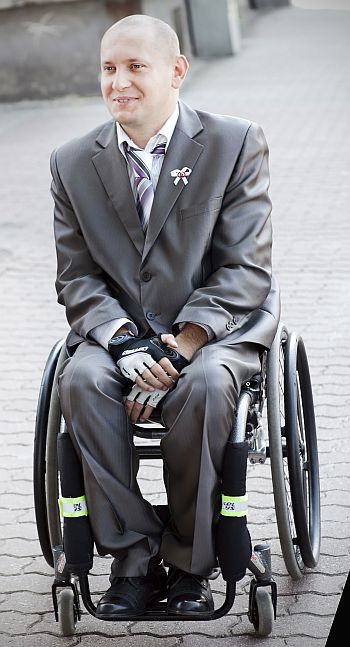 Uśmiechnięty Tomasz Armundowicz siedzi w garniturze na wózku inwalidzkim.