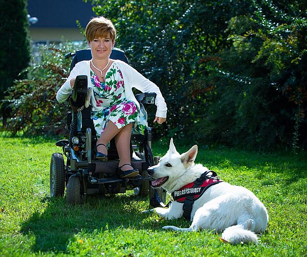 Agnieszka Filipkowska siedzi na wózku elektrycznym, obok niej leży pies asystujący.