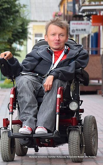 Sebastian Mierzwiński siedzi na wózku elektrycznym, w tle: ulica