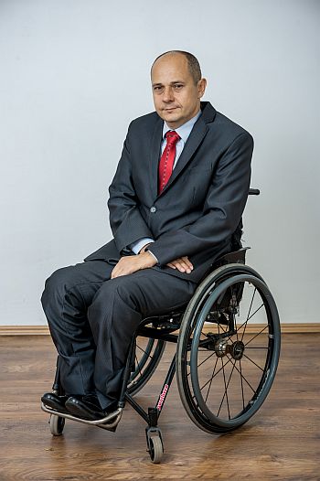 Marek Adam Olszewski siedzący na wózku w eleganckim garniturze