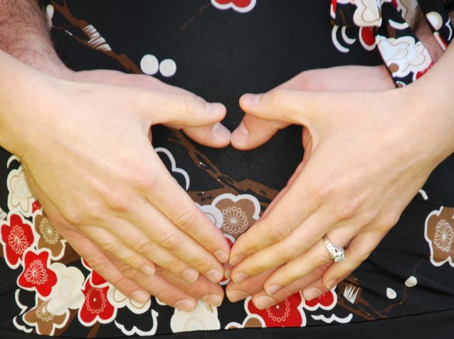 kobieta w ciąży i mężczyzna układają dłonie w kształcie serca na jej brzuchu