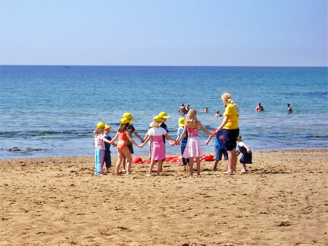 Plaża na brzegu morza. Kobieta stoi w kółku z grupką dzieci