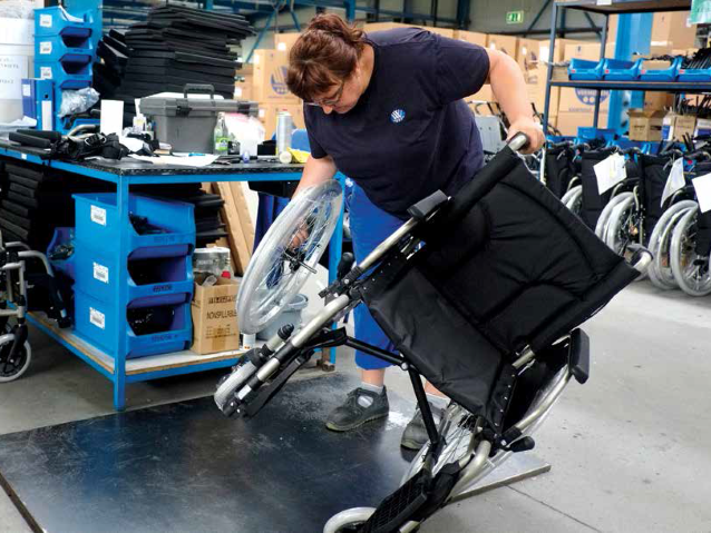 pracownica fabryki przymocowuje koło do wózka inwalidzkiego