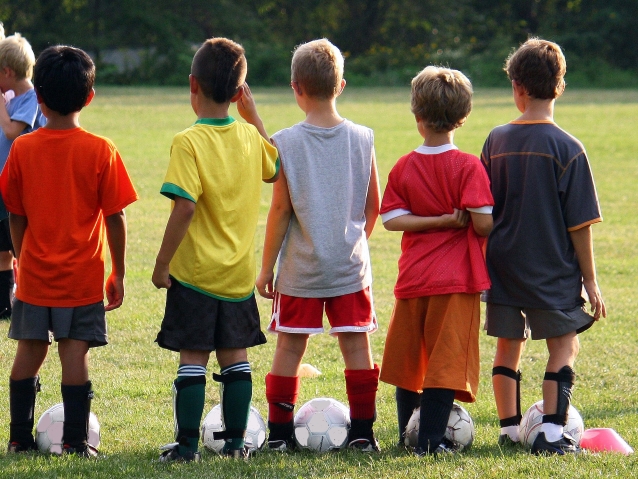pięciu małych chłopców stoi w rzędzie przy piłkach do nożnej