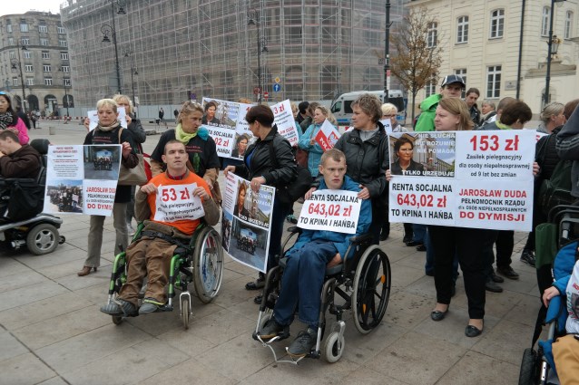 protestujący rodzice z dziećmi z niepełnosprawnością stoją pod Pałacem Prezydenckim