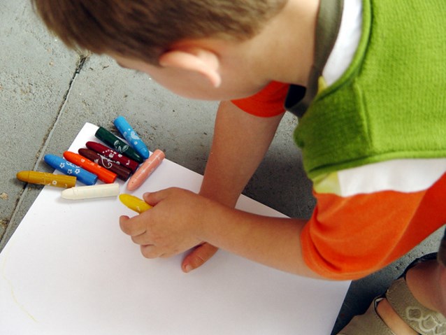 Chłopiec maluje kredkami świecowymi po białej kartce