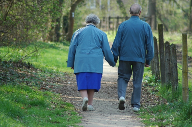 dwoje starszych ludzi idzie polną drogą, trzymając się za ręce
