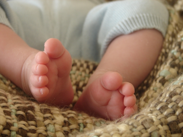 stopy niemowlaka, lezącego na brązowym kocyki