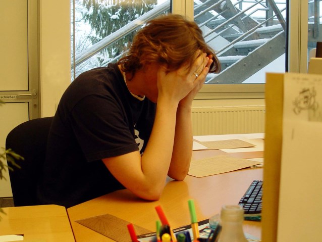 siedząca osoba przy biurku trzyma twarz w dłoniach