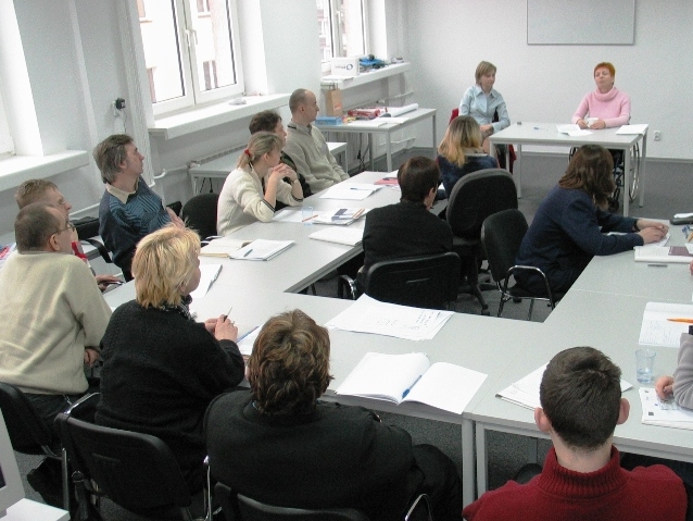 szkolenie w małym pokoju, uczestnicy siedzący przy stolikach słuchający wykładu
