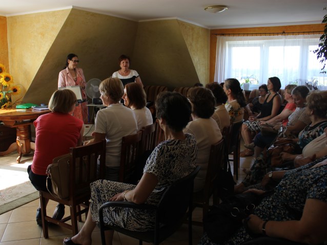 dwie kobiety stoją w pokoju, reszta kobiet siedzi na krzesłach i słucha