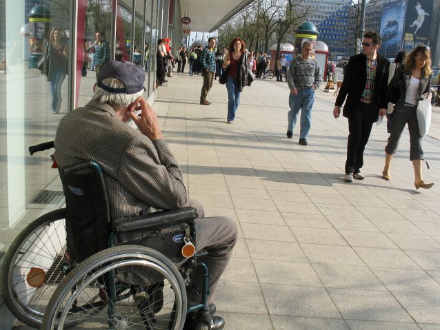 starszy człowiek na wózku przygląda się ludziom