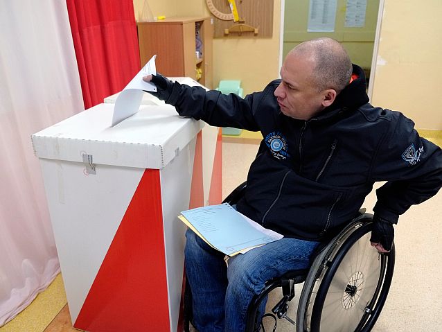 Mężczyzna na wózku wrzuca kartę do głosowania do urny