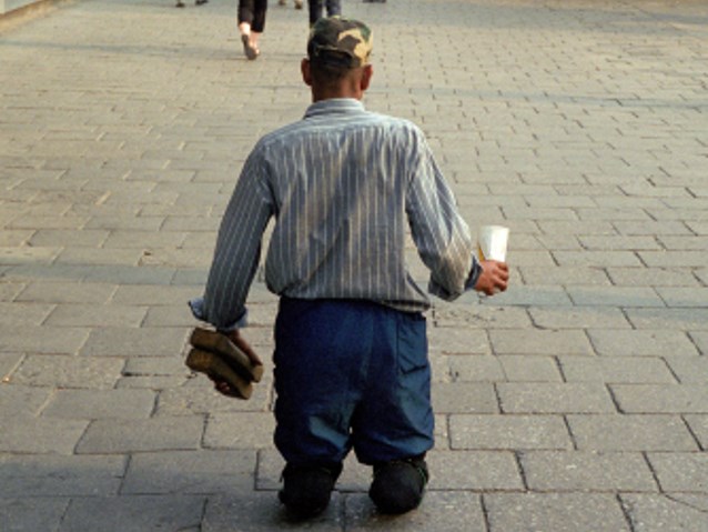 mężczyzna bez nóg klęczy z wyciągniętym kubkiem na chodniku