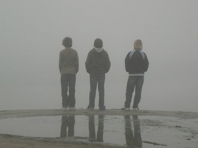 trzech chłopców odwróconych plecami stoi i patrzy przez siebie wśród mgły