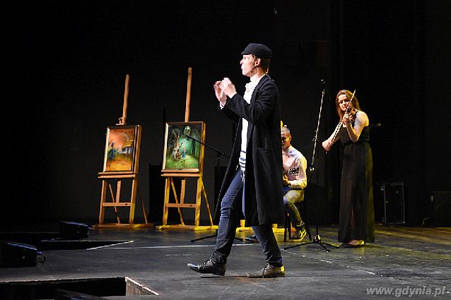 Na scenie: mężczyzna w tradycyjnym ubiorze żydowskim, w tle skrzypaczka i gitarzysta