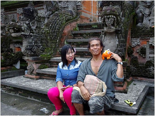 Kobieta i mężczyzna siedzą na schodach, mężczyzna trzyma na ramieniu pluszową maskotkę pomarańczowego kameleona