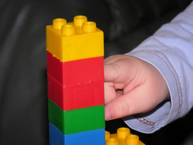 Dłoń małego dziecka dotyka wieży z kolorowych klocków