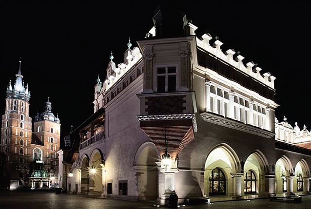 Nocne zdjęcie budynku Sukiennic, w tle Kościół Mariacki w Krakowie