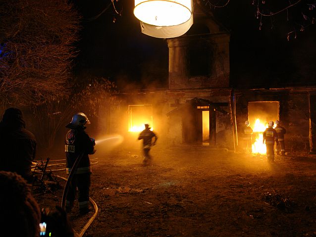 Noc, plan filmowy, strażacy przy płonącym domu, jeden z nich biegnie