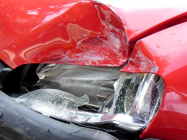 Rozbity przedni reflektor i wgnieciona maska czerwonego samochodu
