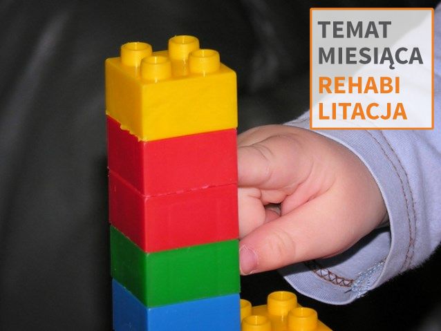 Ręka dziecka dotyka wieży z kolorowych klocków plastikowych. W rogu napis: temat miesiąca: rehabilitacja