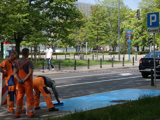 Trzej robotnicy drogowi malują na niebiesko miejsce parkingowe przy ulicy