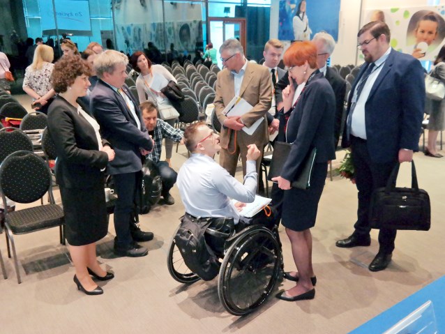Minister Rafalska rozmawia z mężczyzną na wózku w otoczeniu innych osób w trakcie przerwy lub po konferencji