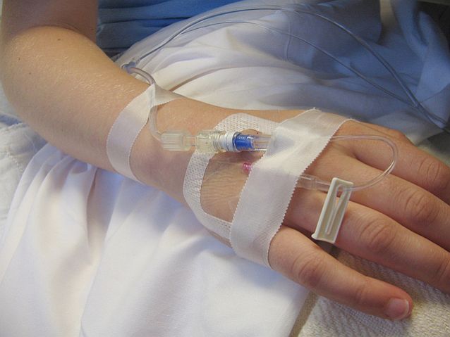 Ręka osoby leżącej w szpitalnym łóżku. W rękę wbity wenflon