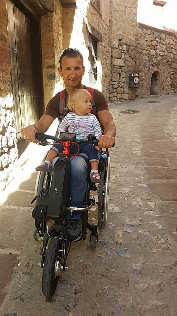 Rafał Szumiec jedzie starą uliczką na wózku z córeczką na kolanach