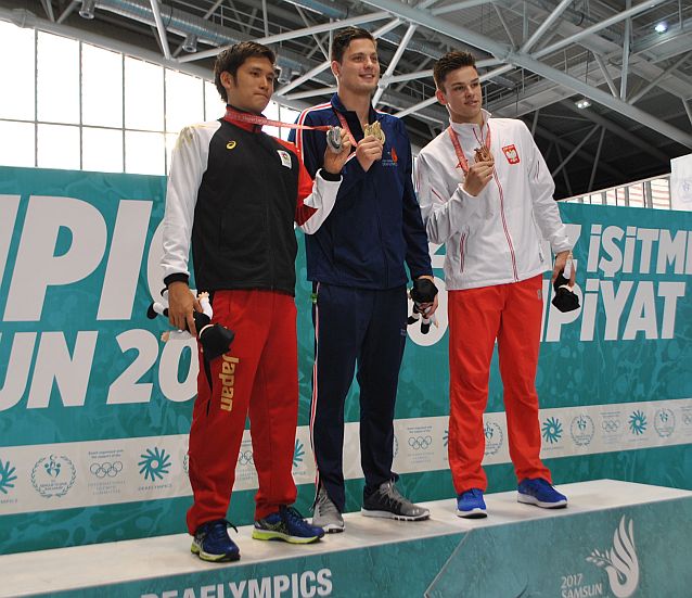 Trzech pływaków stoi na podium prezentując medale. Od lewej: Japończyk, Amerykanin i Polak