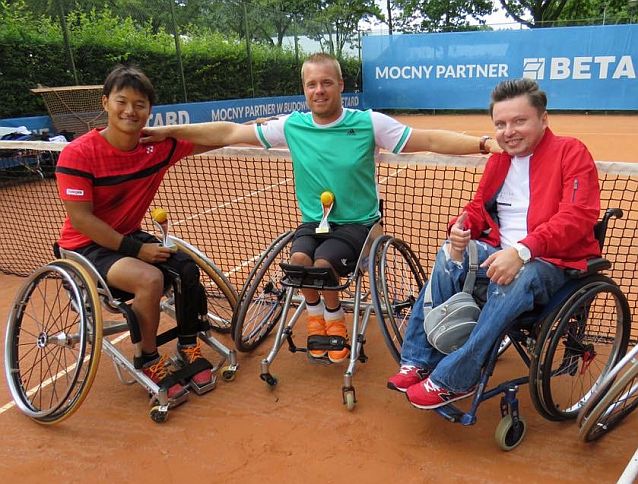 Wspólne zdjęcie przy siatce kortu tenisowego Bartka Skrzyńskiego i dwóch tenisistów - wszyscy na wózkach