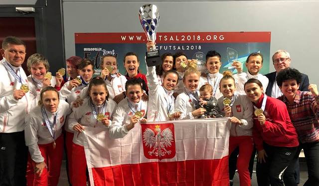 Wspólne zdjęcie całej reprezentacji Polski w futsalu, dziewczyny roześmiane z dumą trzymają złote medale. Kapitan trzyma wysko puchar