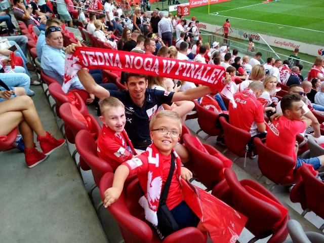 Mężczyzna, z jeden z kibiców trzyma szalik z napisem Jedną nogą w finale, obok niego dzieci z niepełnosprawnością z Amp Futbol Polska