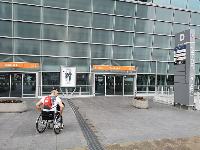 Mężczyzna na wózku przed przeszklonym budynkiem Terminalu A Lotniska Chopina w Warszawie