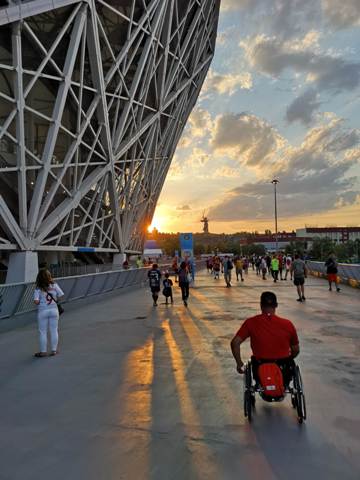 Łukasz Irla jedzie wózkiem przez most, po lewej stronie jest stadion