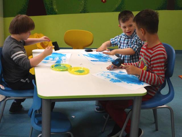 trzech chłopców siedzą przy stoliku i malują niebieską farbą na brystolu