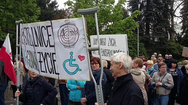 Protest przed Sejmem. Dwoje manifestantów trzyma transparent zawieszony na kulach