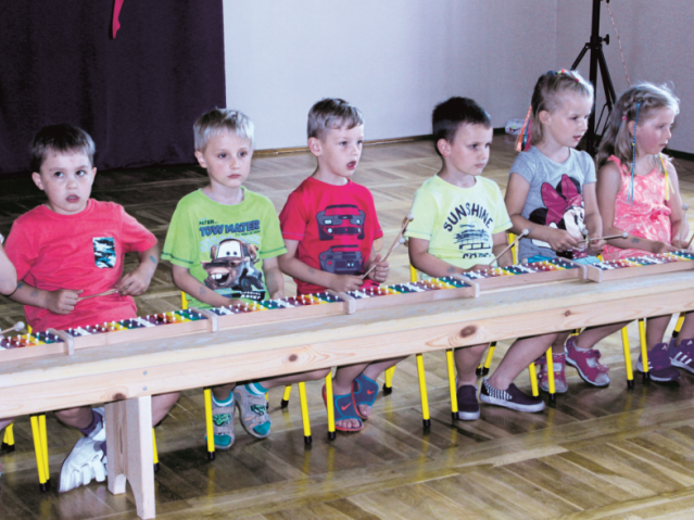 przedszkolaki siedzą przy długim stoliku, każdy z nich ma swoje cymbałki
