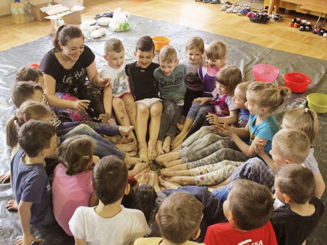 przedszkolaki wraz z przedszkolanką siedzą na podłodze w kole, wszyscy stykają się stopami