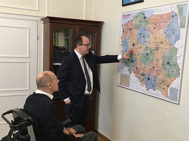 Wnętrze gabinetu. Adam Bodnar pokazuje siedzącemu na wózku Piotrowi Pawłowskiemu wisząca na ścianie mapę Polski