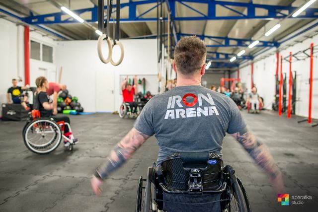 Mężczyzna na wózku od tyłu w siłowni. na jego koszulce na plecach jest napisane Iron Arena