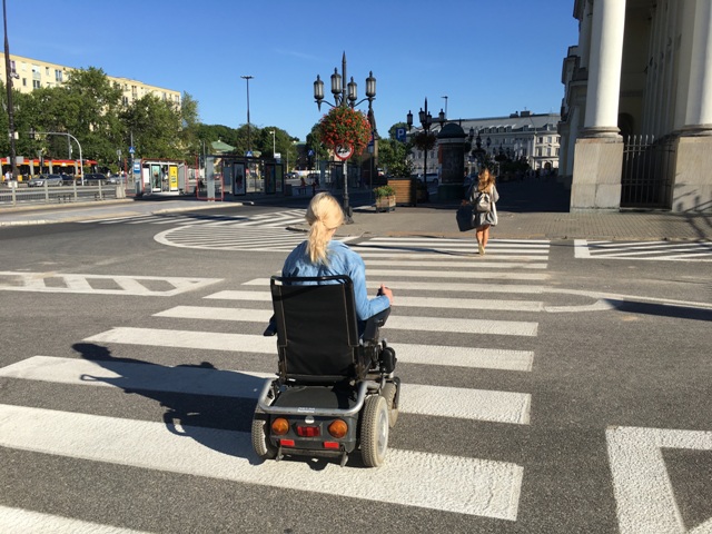kobieta poruszająca się na wózku elektrycznym przechodzi przejście dla pieszych przy pl. Bankowym w Warszawie