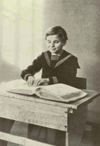 chłopak ok. 10-12-letni siedzi w mundurku w ławce, uśmiechnięty czyta książkę w braillu