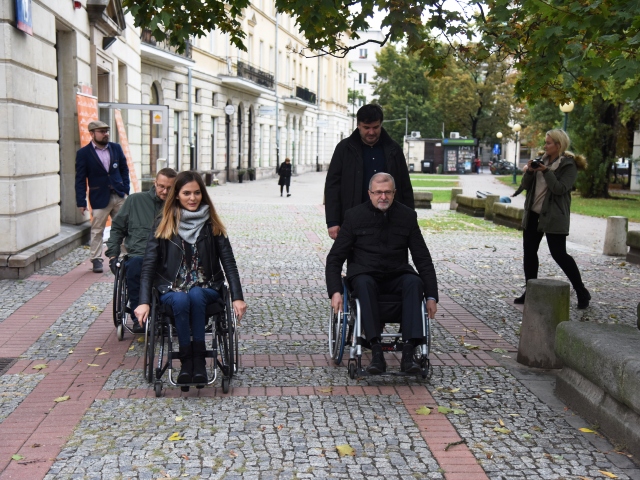 Sławomir Antonik tuż przed siedzibą Integracji jedzie na wózku, obok niego insrtuują kobieta i mężczyzna poruszający się na wózku, z tylu idzie asekurant