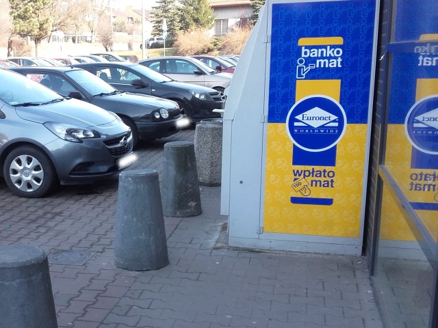 Bankomat na chodniku blokuje przejście, tuż obok zaparkowane samochody