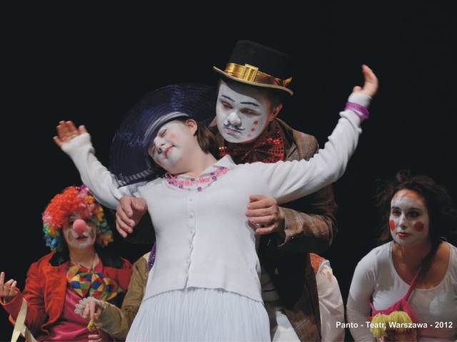 aktorzy w przebraniach scenicznych na scenie dziewczyna z zespołem downa oparta plecami o aktora w kapeluszu