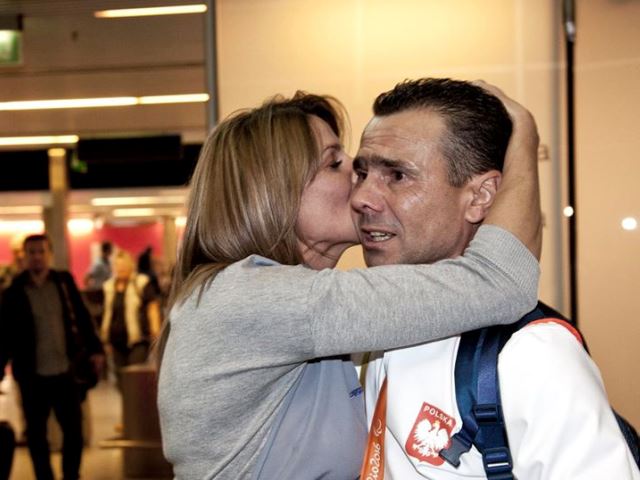 Jacek Gaworski i jego żona witają się na lotnisku, żona całuje męża w policzek i przytula
