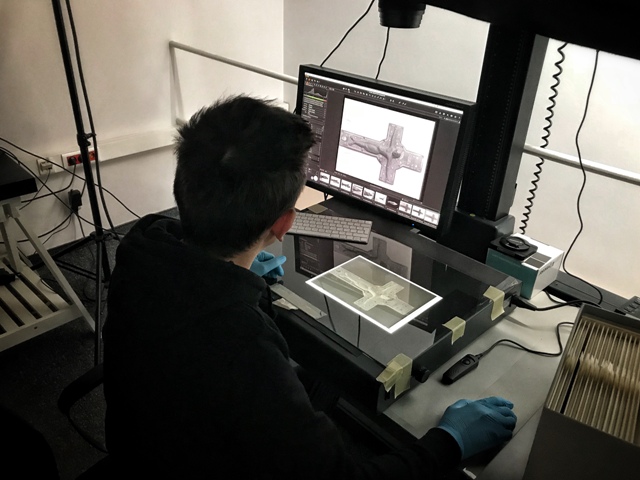 pracownik muzeum pracuje przy komputerze nad stroną internetową na rękach ma rękawice gumowe siedzi tyłem